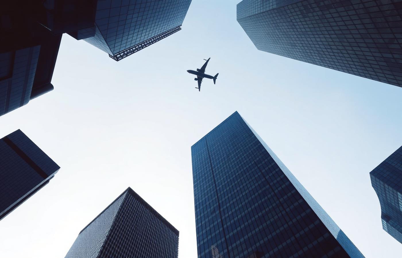 Glass towers seen from below with an aircraft crossing the sky