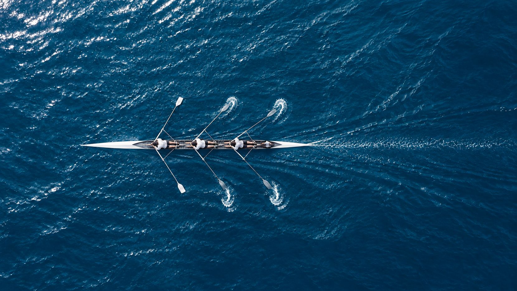 Aerial view of a single rowing boat cutting a clean line through dark water